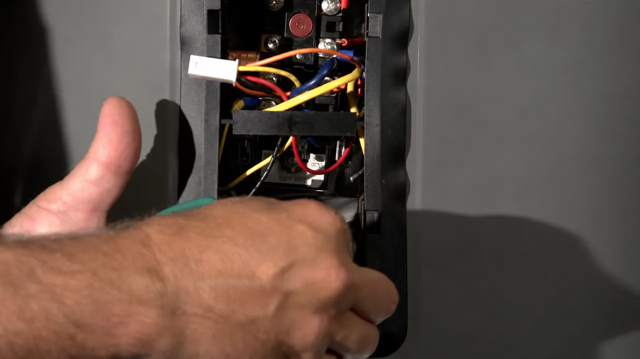 Hands beside wiring and controls in an electric water heater