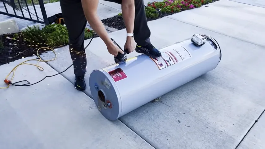Person working on a water heater tank on an outdoor concrete driveway
