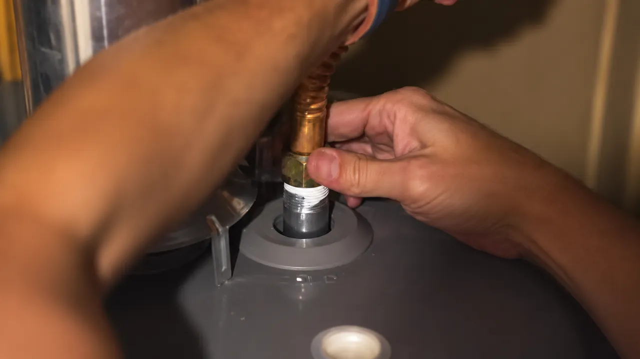 Hands fitting a water connection at the top of a storage water heater
